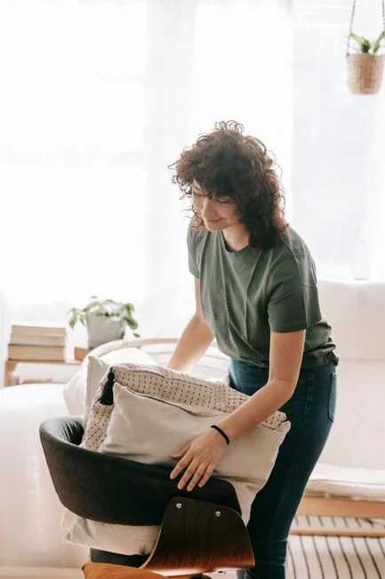A hotel housekeeper neatly stacks fresh towels in a luxurious room setting.